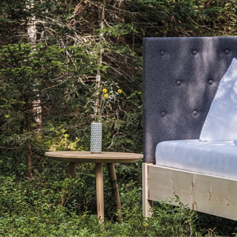 Holzbett der Tischlerei Weissteiner mit gepolsterter Rückenlehne und kleinem, runden Tisch