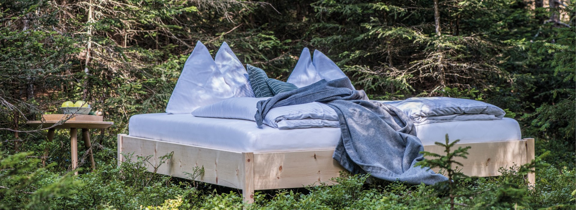 Doppelbett aus Holz mit rundem Tisch inmitten der Natur